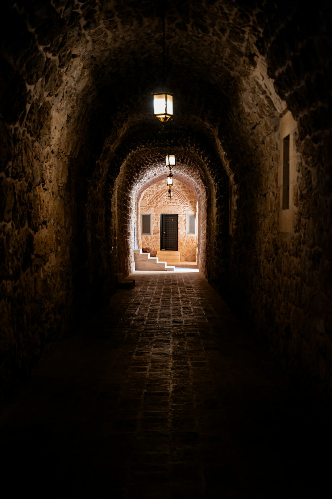 Old wooden door slightly open in a dim stone corridor with a single hanging light
